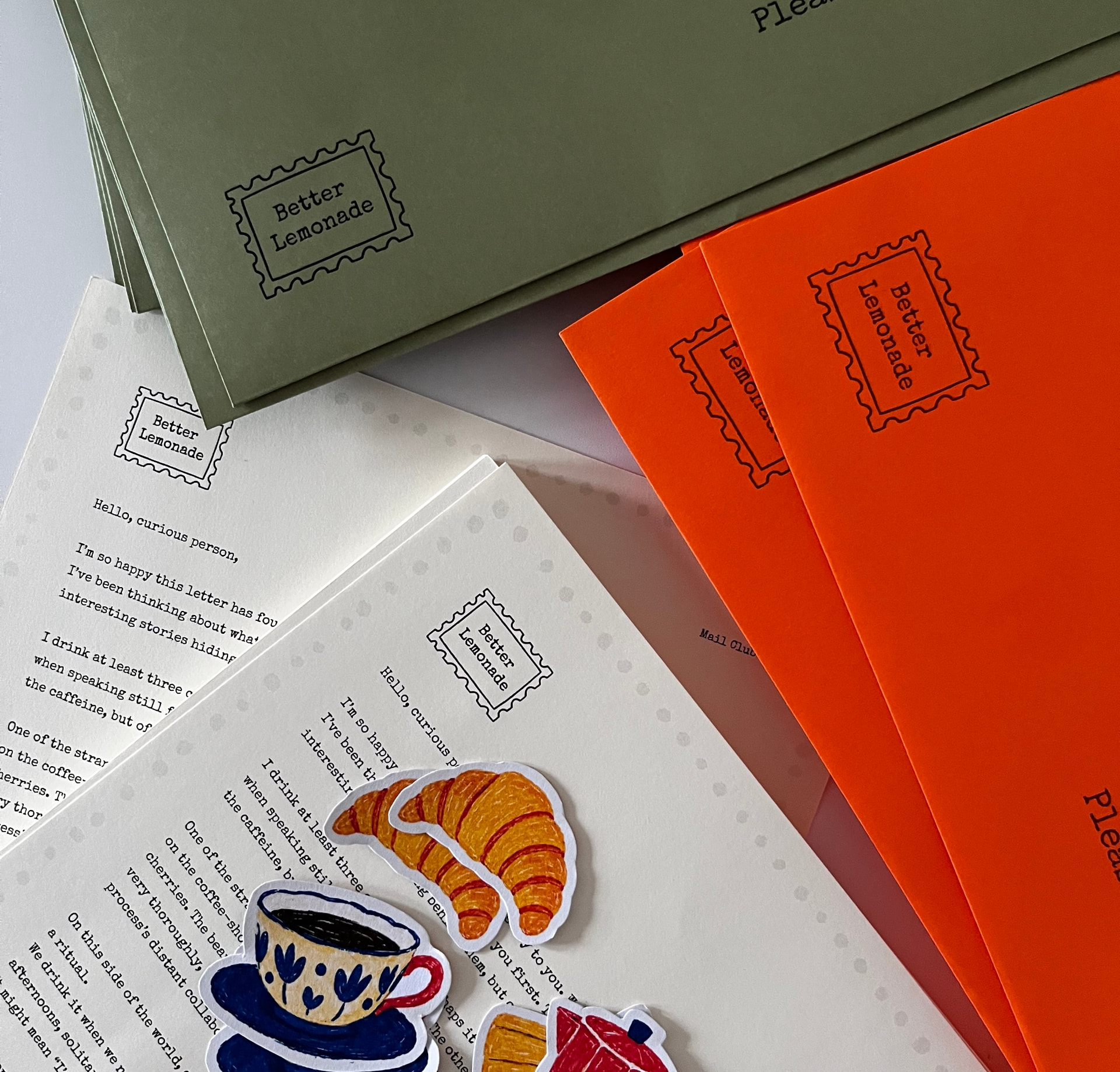 Olive and orange Better Lemonade envelopes with typewritten letters and hand-drawn croissant and coffee cup stickers
